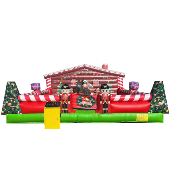 A large inflatable Christmas bounce house features a festive gingerbread house design with red and white stripes. Nutcracker figures stand at either side of a decorative sign that reads "Merry Christmas." A gray mechanical reindeer is positioned in the center, surrounded by colorful holiday accents, including ornaments.